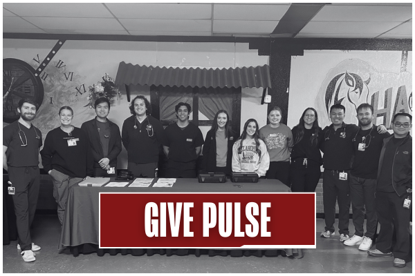 Black and white image of students smiling behind a table of resources at an outreach event. Title on image says "Give Pulse".