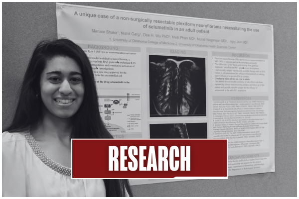 Black and white image of a student smiling in front of their research poster at the Unity Week student-led poster hall. Title on image says "Research".