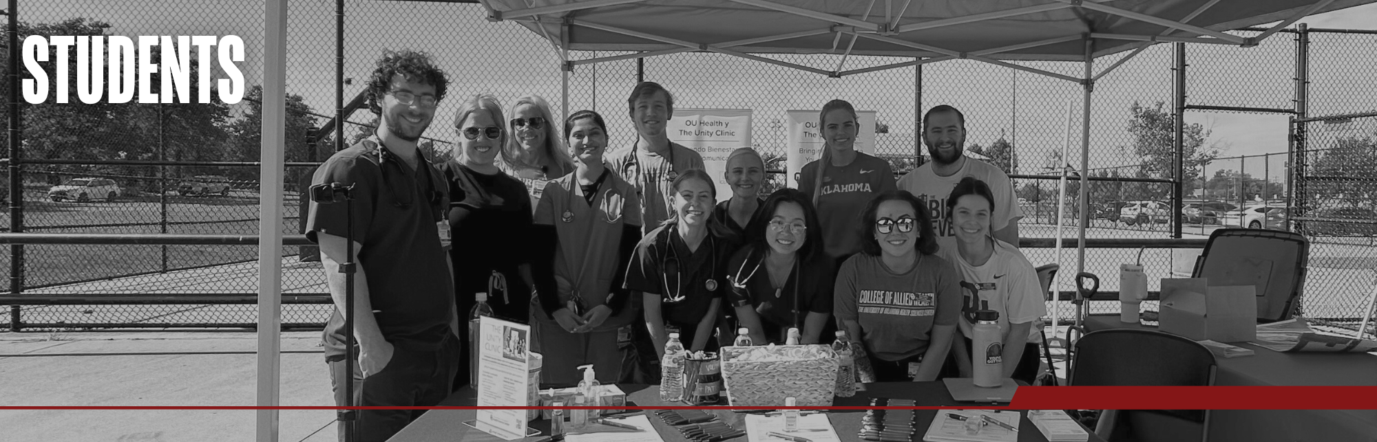 Black and white image of students smiling gathered around an Unity Clinic outreach booth. Title on image says "Students".